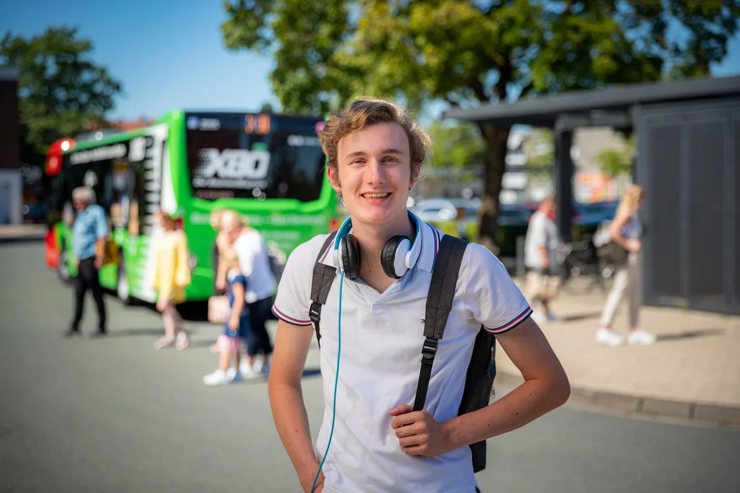 Junge mit weißem Poloshirt steht vor einem grünen X80 Bus